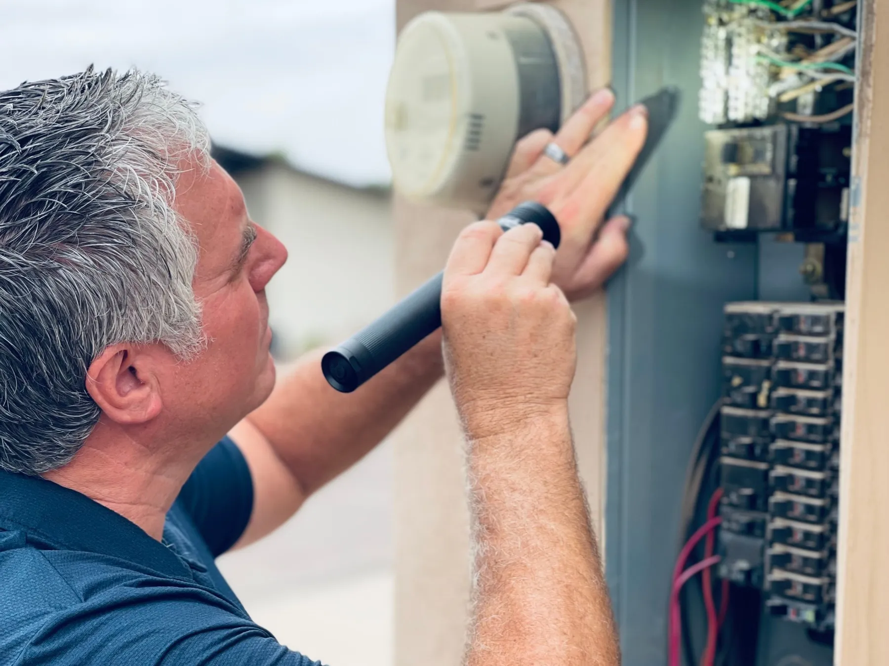 Bob Clardy using a flashlight to inspect an open exterior electrical service panel